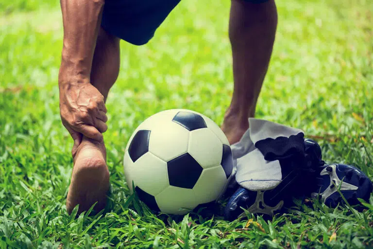 Close-up of a soccer ball with a man standing behind it, grasping his ankle.