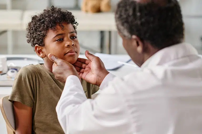 A provider feels the glands in a boy’s neck during a sore throat exam.